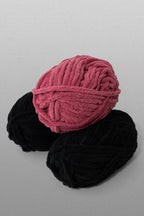 Two skeins of yarn, one pink and one black, on a gray background
