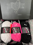 Three skeins of yarn in white, pink, and black with Defiant Yarn labels on a gray background.