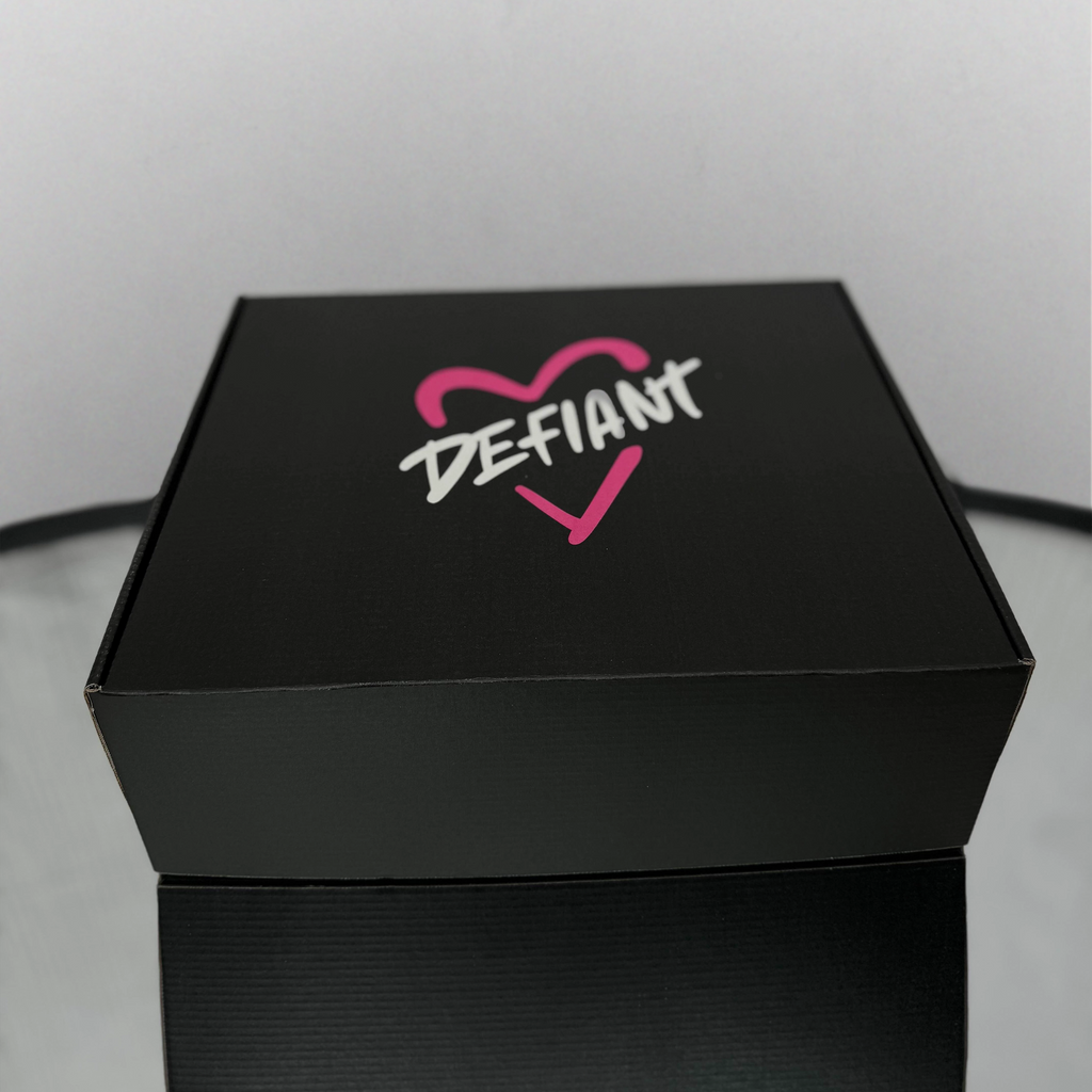Black box with 'DEFIANT' logo featuring a pink heart on a light gray background