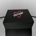 Black box with 'DEFIANT' logo featuring a pink heart on a light gray background