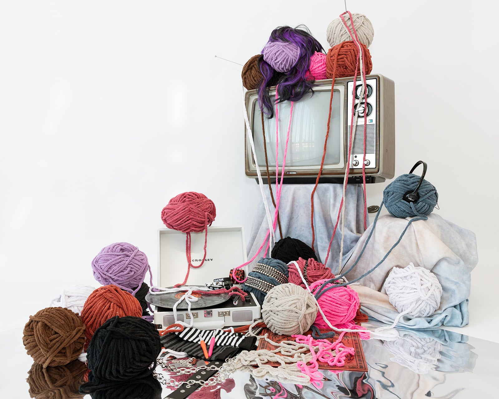 Colorful yarn balls and knitting materials on a table with an old television set in the background.