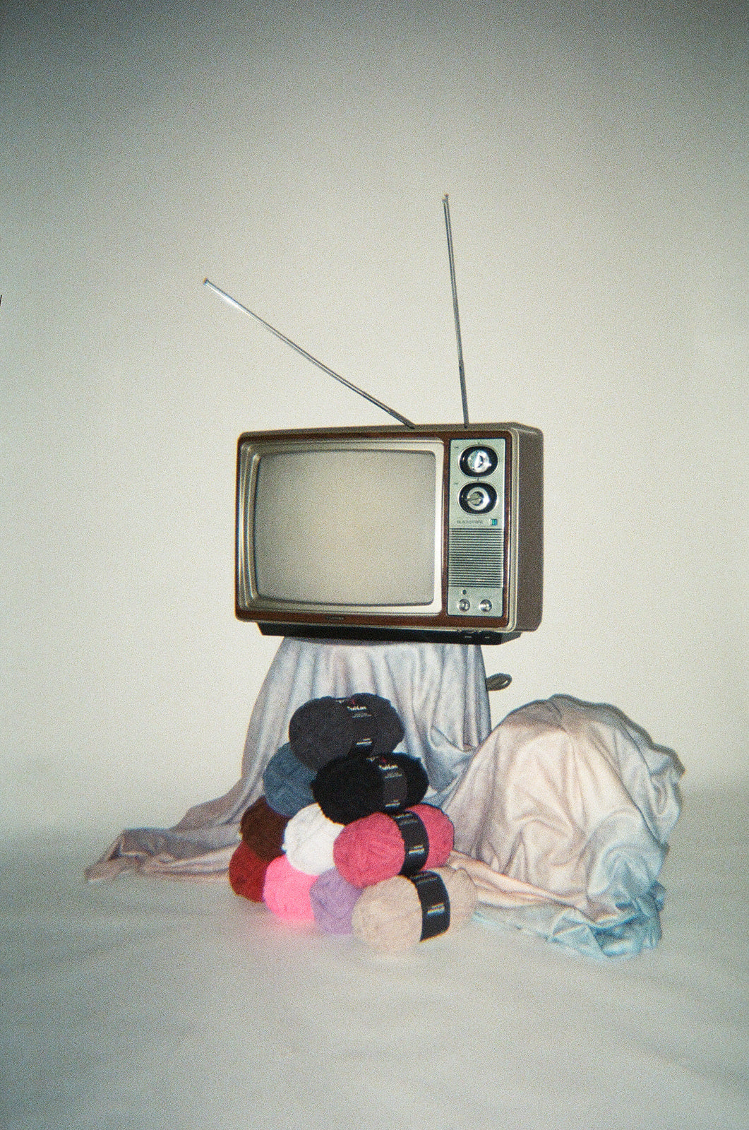 Vintage television with yarn balls and fabric on a plain background