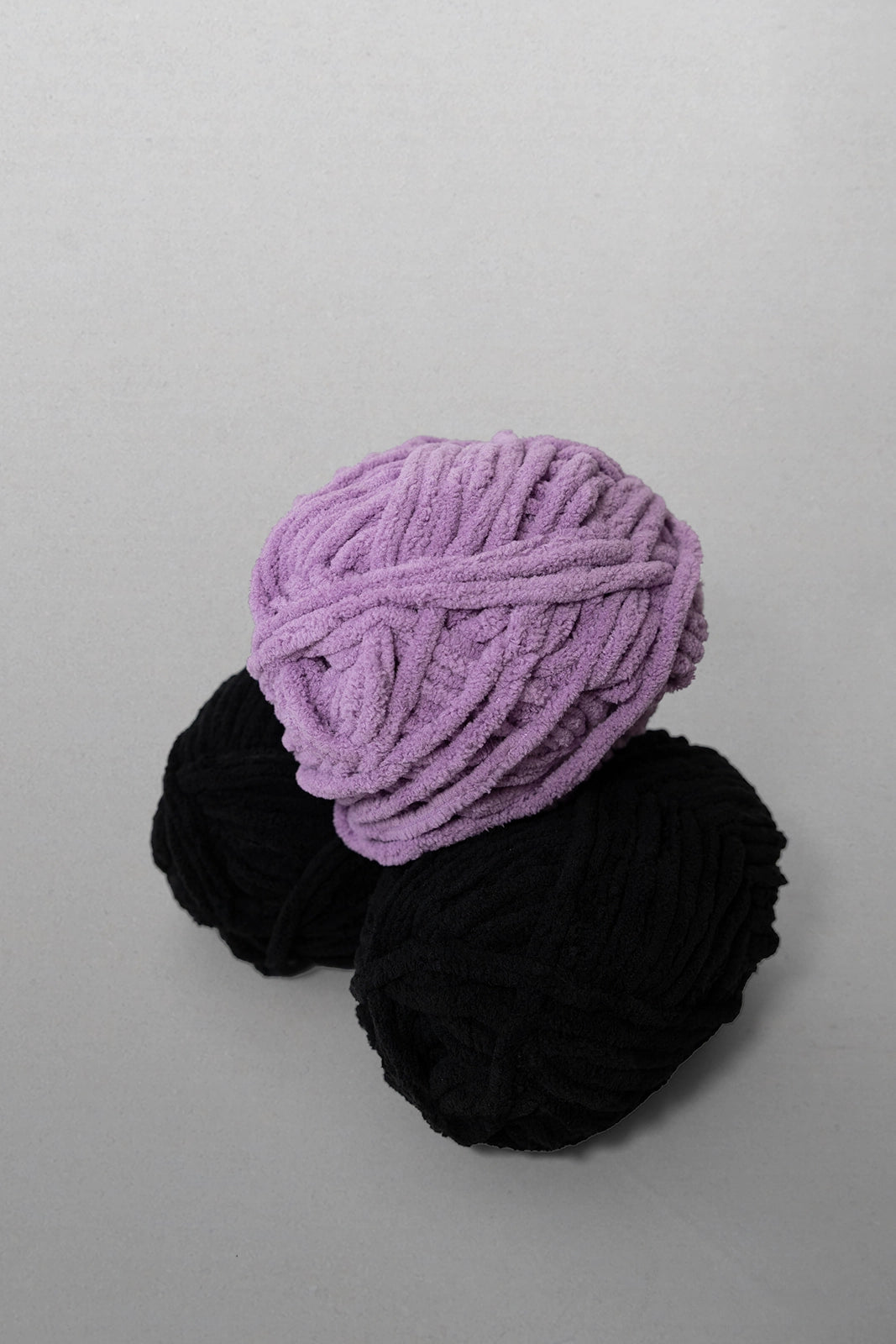Two balls of yarn, one purple and one black, on a light gray background