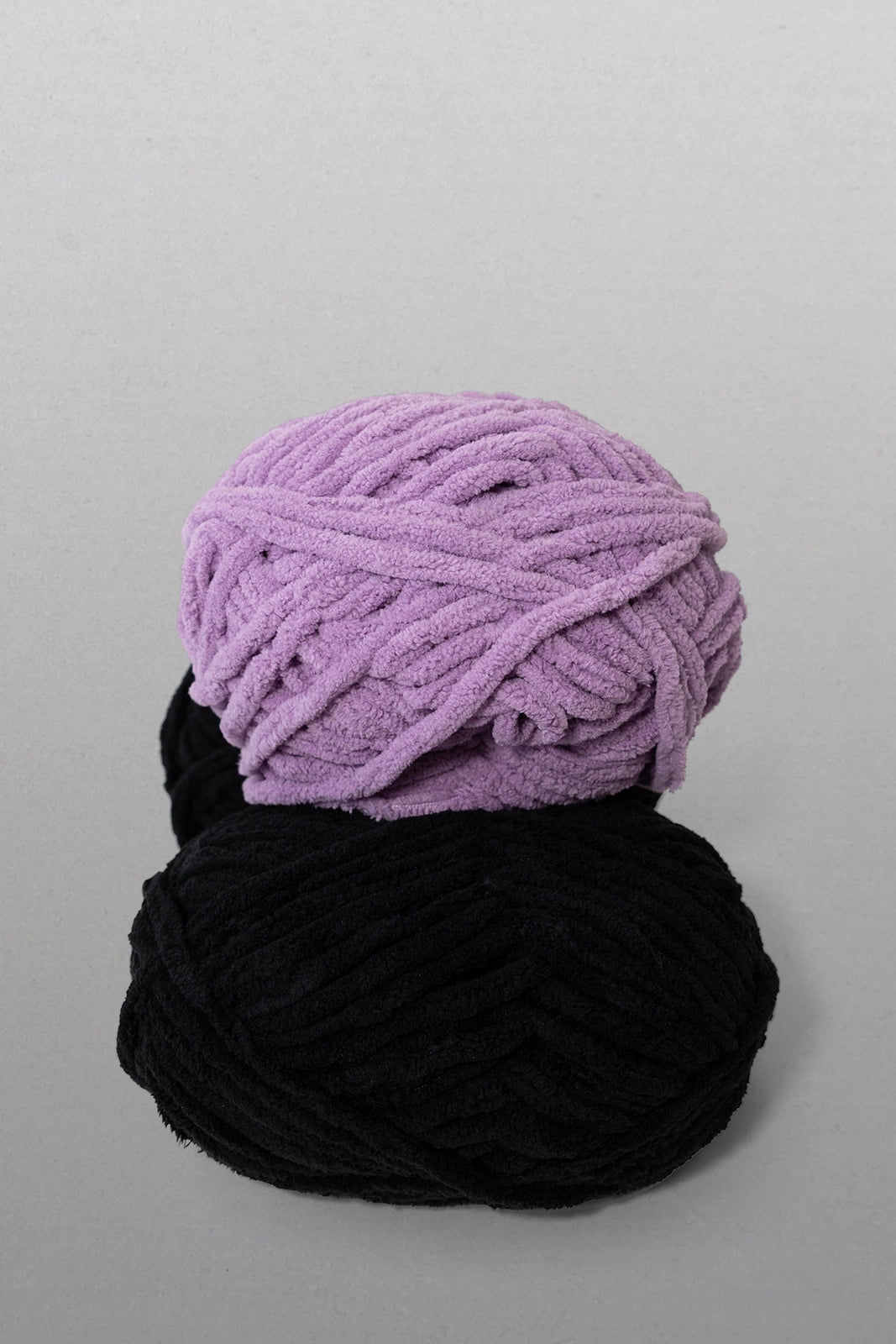 Two balls of yarn, one purple and one black, on a gray background