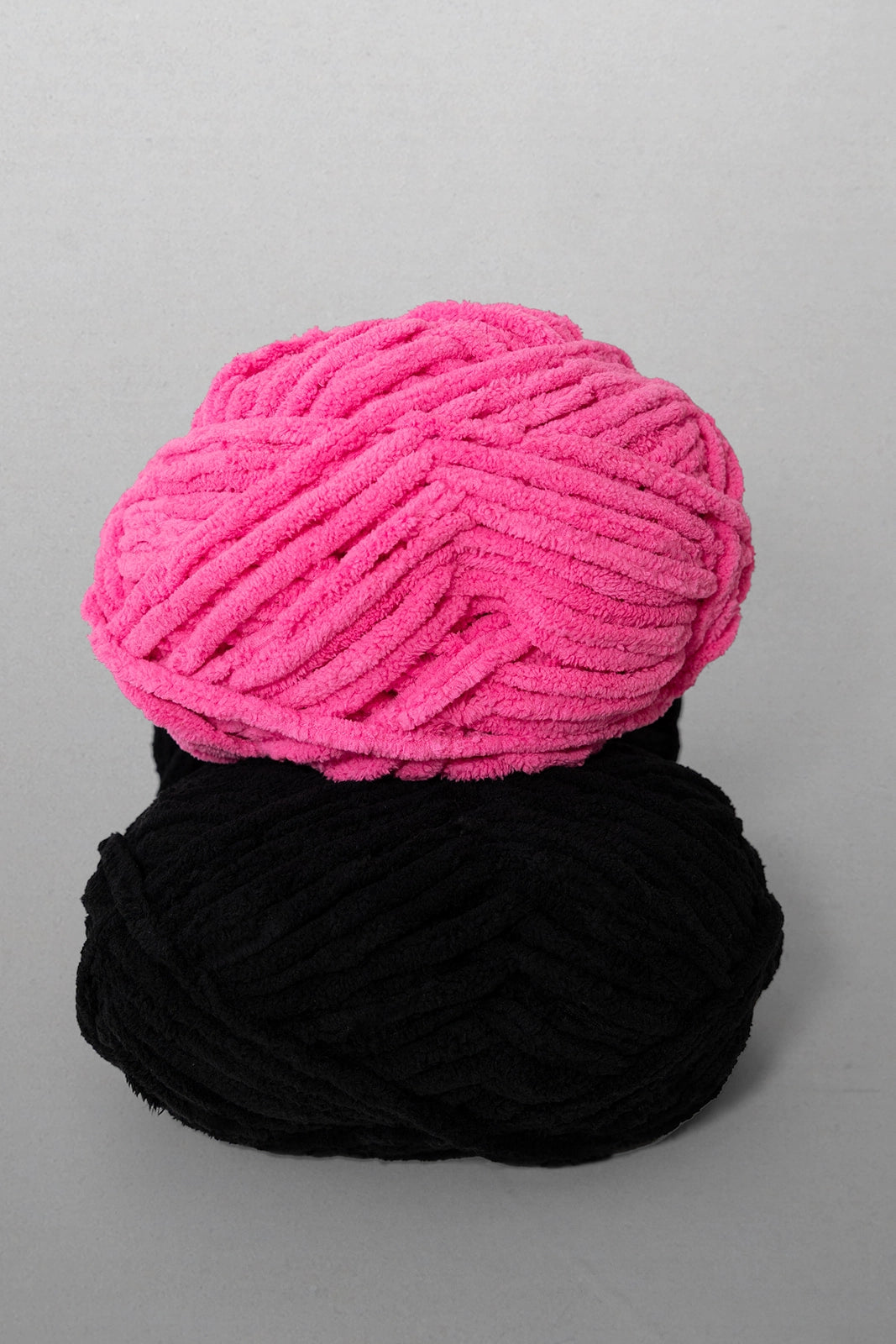 Two skeins of yarn, one pink and one black, on a gray background