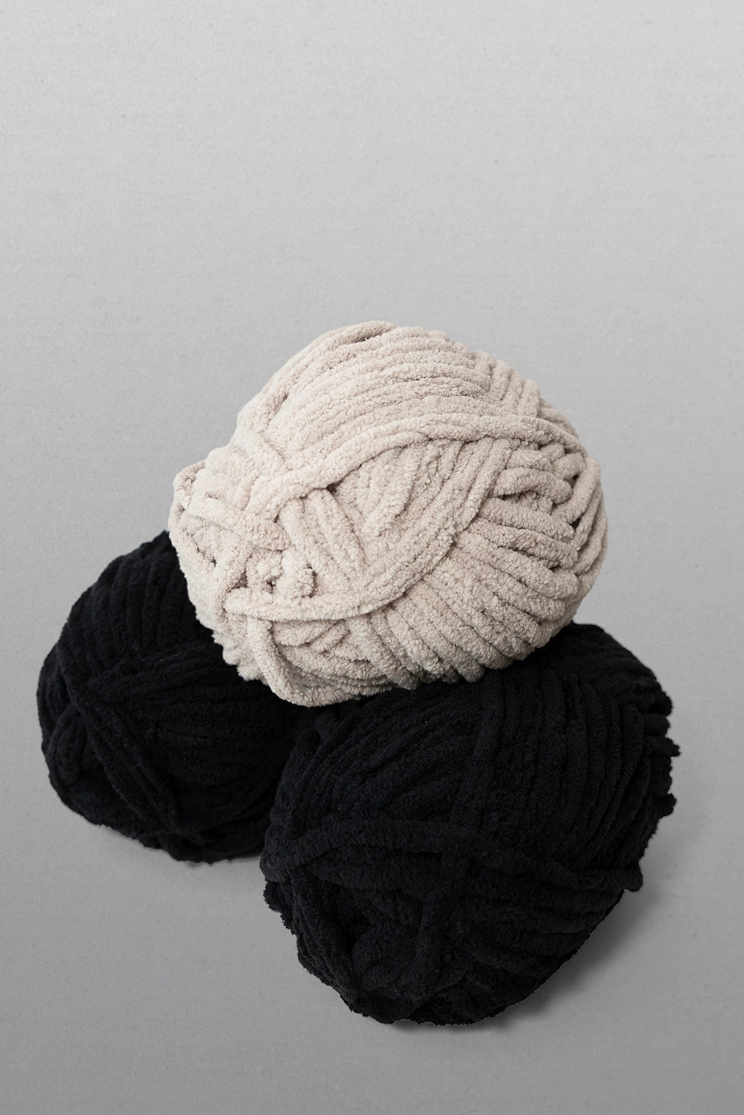 Three balls of yarn in black and beige on a gray background