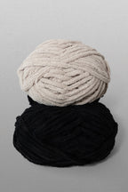 Two skeins of yarn, one black and one beige, on a gray background