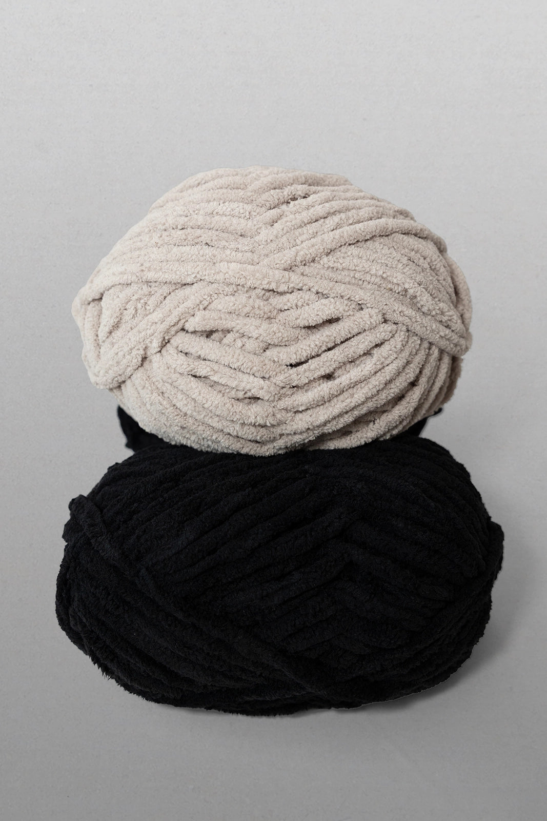 Two skeins of yarn, one black and one beige, on a gray background