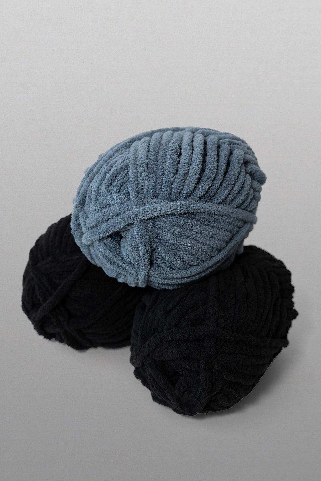 Two balls of yarn, one blue and one black, on a light gray background.
