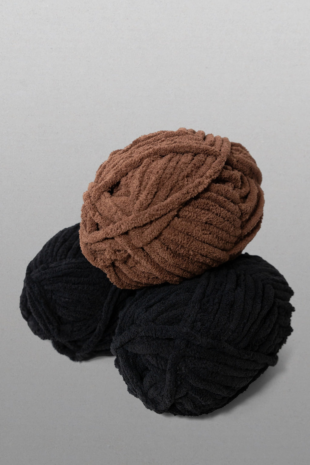Two balls of yarn, one brown and one black, on a gray background