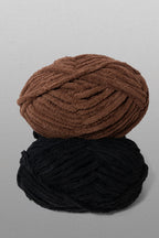 Two skeins of yarn, one brown and one black, on a gray background